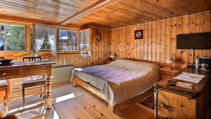 Une chambre dans un chalet en bois, avec un lit, un bureau et une fenêtre donnant sur une forêt.