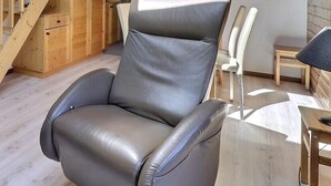 Uma sala de estar moderna com um sofá de couro cinzento, uma poltrona de couro, uma escada de madeira e uma pequena mesa de madeira.