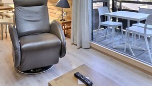 Quarto moderno com poltrona de couro, mesa de jantar de madeira e varanda com cadeiras brancas.