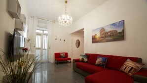 A modern living room with a red sofa, a red armchair, a chandelier, a flat-screen TV, and a painting of the Colosseum. - FLAMINIA STREET APARTMENT (Roma)