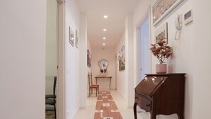 A hallway with a patterned carpet, a wooden side table with a vase, and framed pictures on the wall. - FLAMINIA STREET APARTMENT (Roma)