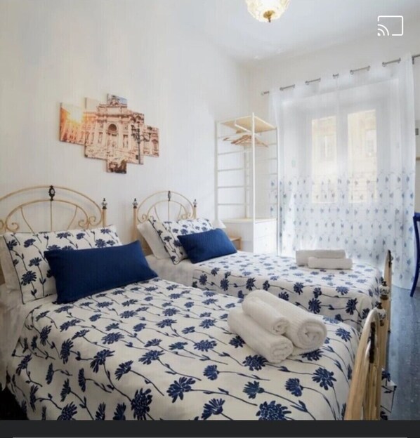 Two plush beds are flanked by nightstands and a headboard, with a shelf unit and framed picture adding to the room's charm.