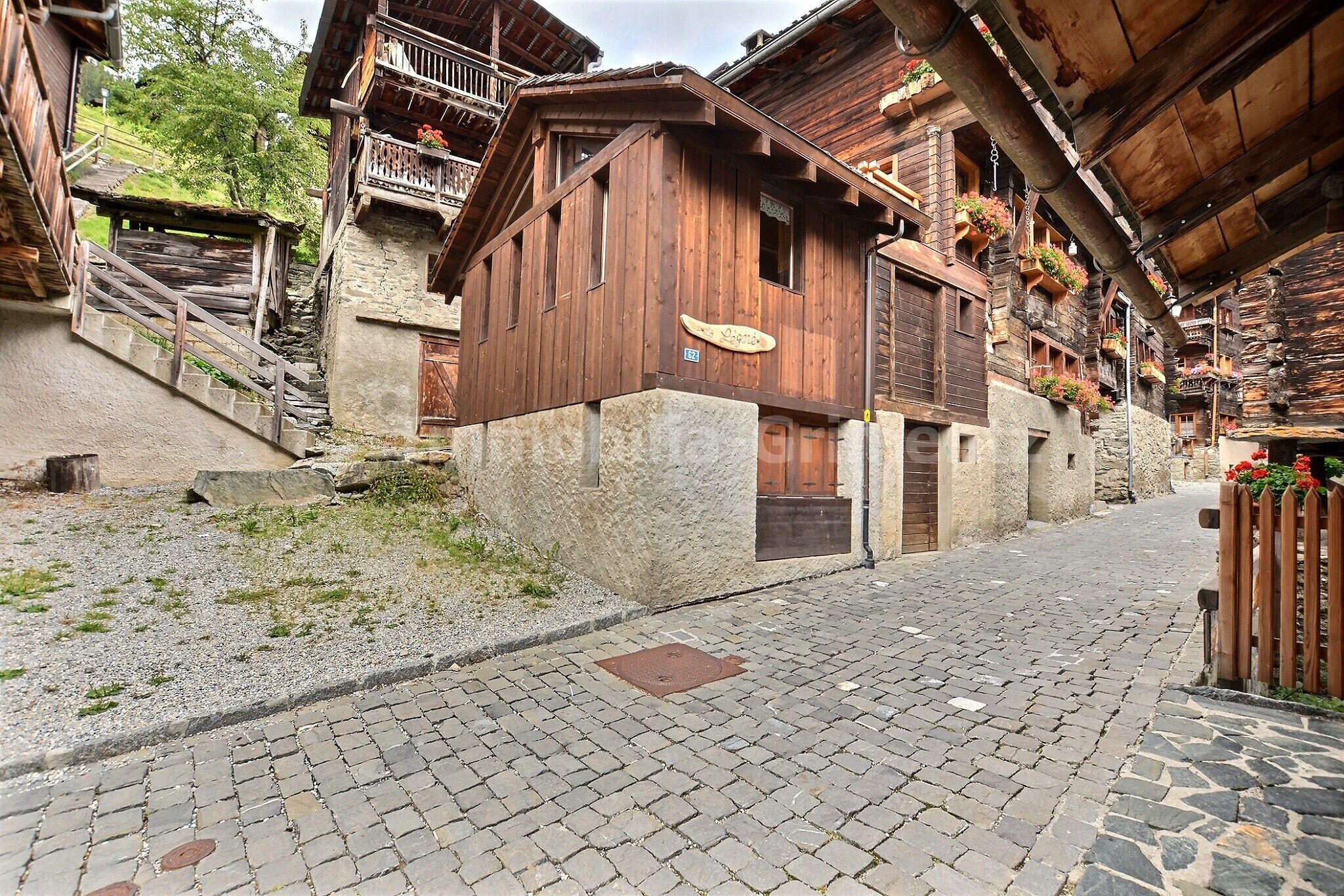 Eine enge Kopfsteinpflasterstraße, gesäumt von traditionellen Holzbauten mit Balkonen und Blumenkästen.