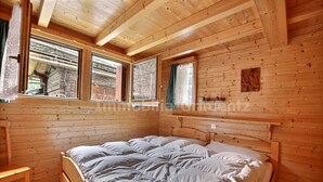 A wooden cabin bedroom with a bed, two windows, and a wooden headboard.