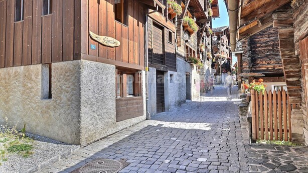 A narrow cobblestone street flanked by traditional wooden buildings with balconies and flower boxes.