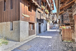 A narrow cobblestone street flanked by traditional wooden buildings with balconies and flower boxes.