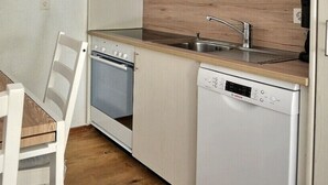 A compact kitchen with a wooden table, white chairs, a Bosch dishwasher, a built-in oven, and a sink. - Comfortable studio for 2 people, living room with 1 double bed, kitchen area with dishwasher, bath-W (Grimentz)