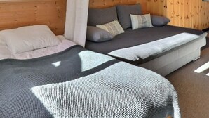 Et værelse med to senge, en sofa, et spisebord med stole og et lille tekøkken.
