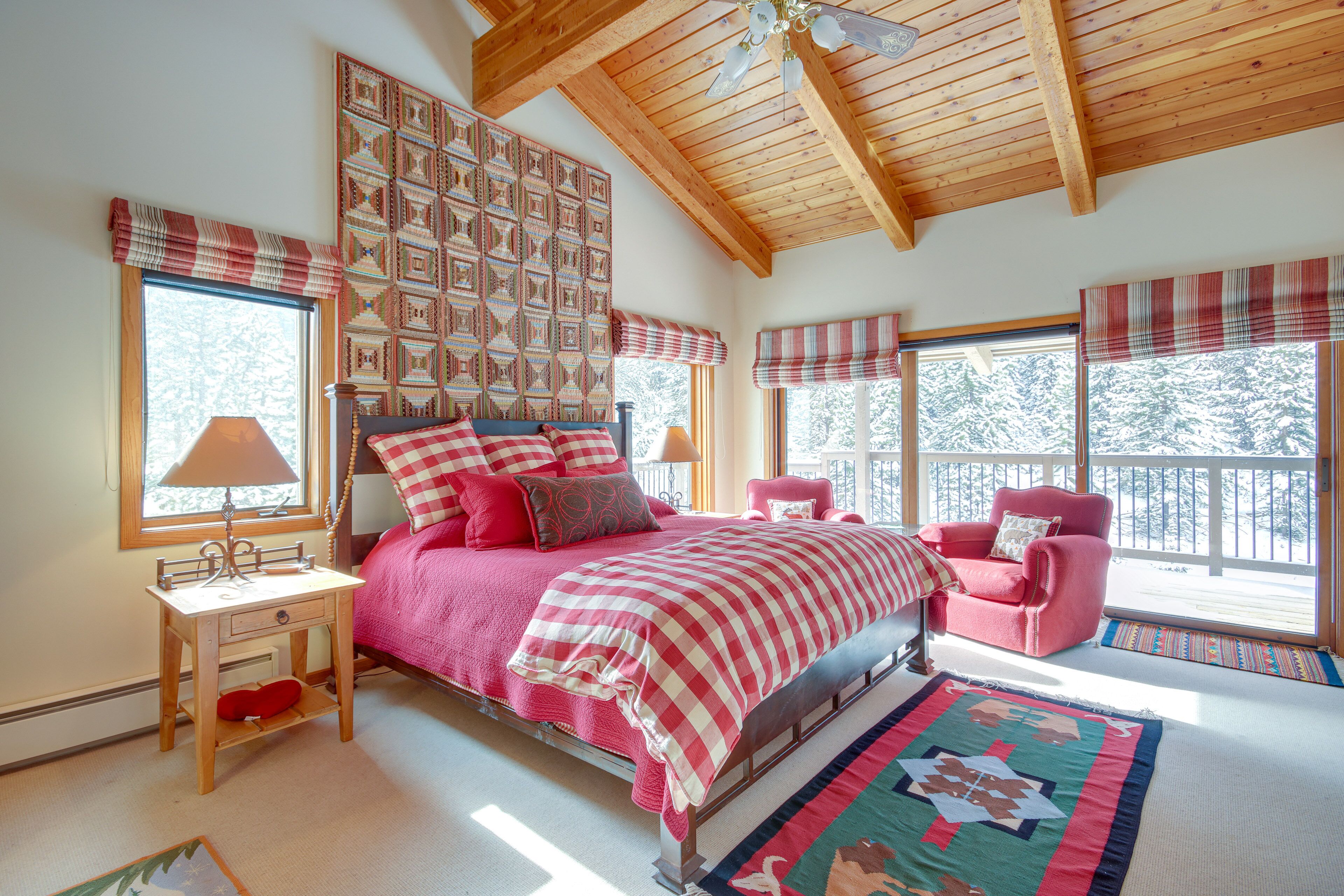 Ein Schlafzimmer mit Holzbalkendecke, einem Bett mit rot-weißer Karodecke, einem rosa Stuhl und einer gesteppten Wandtasche.