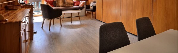 Een moderne keuken met houten kasten, een eethoek met een tafel en stoelen, en een gezellige zithoek met een bank en kussens.