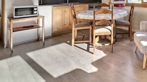 A cozy room with a wooden dining table, chairs, a plaid armchair, a bed, and a microwave on a small table.