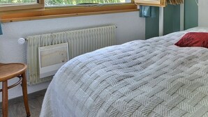 A bedroom with a bed, two pillows, a chair, and a window with a view.
