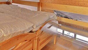 En säng av trä med ett vitt täcke i ett rum med träväggar och trägolv.