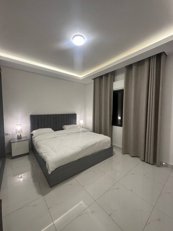A modern bedroom with a large bed, bedside lamps, a ceiling light, and a view of the outdoors through a window.