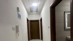 A hallway with a tiled floor, a wooden door at the end, and a light fixture on the ceiling. - JRE Cozy Home Near All Services 20 (Amman)
