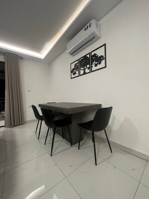A modern dining area with a dark-toned table and four black chairs, an air conditioning unit, and three framed tree silhouettes on the wall.