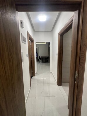 Un couloir avec des portes en bois, un luminaire au plafond et un sol carrelé.