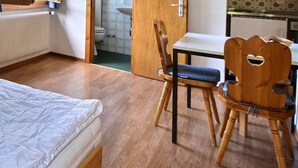 Una stanza con un letto, una sedia, un tavolino e un termosifone.