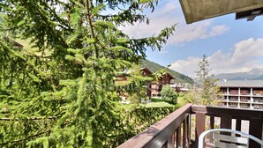 Un balcone con ringhiera in legno, un tavolo in metallo e vista su un paesaggio montuoso con edifici sullo sfondo.