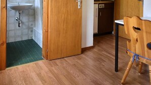 Una stanza con pavimento in legno, un tavolo da pranzo con sedie, un lavandino e una porta che dà su un'altra stanza.