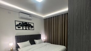 Un dormitorio moderno con una cama, mesitas de noche, aire acondicionado de pared y una lámpara de techo.