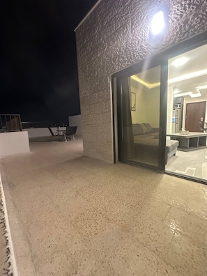 Edifício moderno com fachada texturizada e entrada por porta de vidro, revelando um interior com cozinha e área de estar.