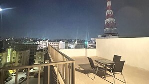 Una terraza en la azotea con una mesa y sillas, vistas a un paisaje urbano y una torre alta a lo lejos.