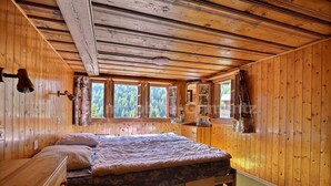 Ein Schlafzimmer einer Holzhütte mit einem Bett, einem Schminktisch und einem Fenster mit Blick auf einen Wald.