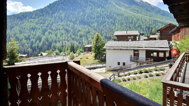 Blick auf ein Gebirge mit einem Holzhaus und einem kleinen weißen Gebäude im Vordergrund.