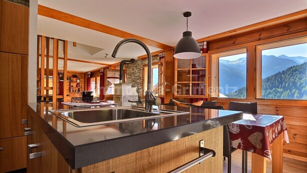 Une cuisine moderne dotée d’un grand îlot central, de meubles en bois et offrant une vue sur les montagnes grâce à de grandes fenêtres.