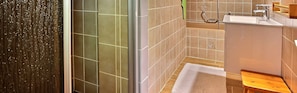 Un baño con ducha, lavamanos y banco de madera.