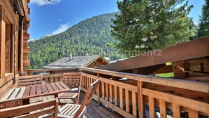 Une terrasse en bois, dotée de tables et de chaises, qui offre une vue sur une montagne boisée.