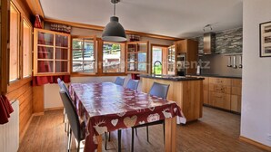 Un coin repas avec une table recouverte d’une nappe à motifs, des meubles de rangement en bois et une cuisine dotée d’un pare-feu en pierre.