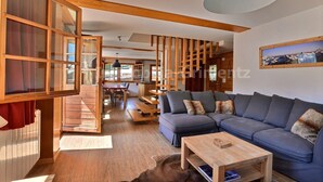 Un salon moderne avec un canapé d’angle, des poutres en bois et un coin repas.