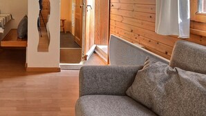 A cozy room with a wooden floor, a grey sofa, a small round table with a plant, and a bed with a striped bedspread. - Comfortable studio for 2 people, living room with 2 beds, kitchen area with dishwasher, shower-WC, s (Grimentz)