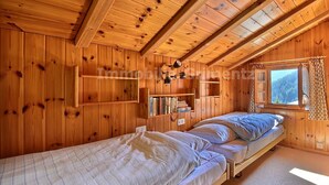 A wooden cabin room with a loft bed, a shelf with books, and a window with curtains. - Comfortable flat on 2 levels for 3 to 4 people, living room, kitchen area, 1 double bedroom (140), 1 (Grimentz)
