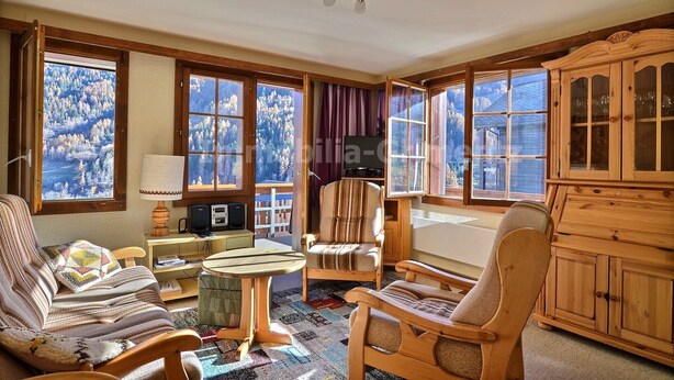 Ein gemütliches Zimmer mit großen Fenstern, Holzmöbeln und Blick auf eine verschneite Landschaft.