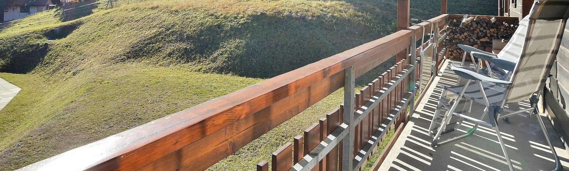 A balcony with a wooden railing overlooking a grassy hill.