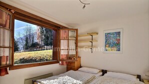 Ein Schlafzimmer mit großem Fenster, einem Bett, einem Nachttisch, einem Regal und einem Bild an der Wand.