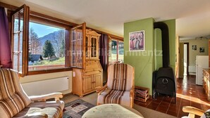 Ein gemütliches Wohnzimmer mit großem Fenster, Kaminofen und Blick ins Freie.