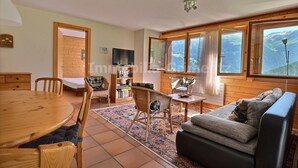 Ein gemütliches Wohnzimmer mit Holzboden, einem Esstisch, einer Couch und einem Fernseher.
