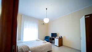 A hotel room with a bed, a desk, a chair, a television, and an air conditioning unit. - Hotel Parnaso (Trebisacce)