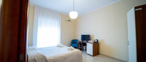 A hotel room with a bed, a desk, a chair, a television, and an air conditioning unit.