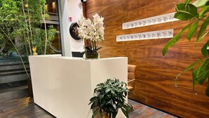 A reception desk with a white surface, a clock, and two potted plants. - Hotel Parnaso (Trebisacce)