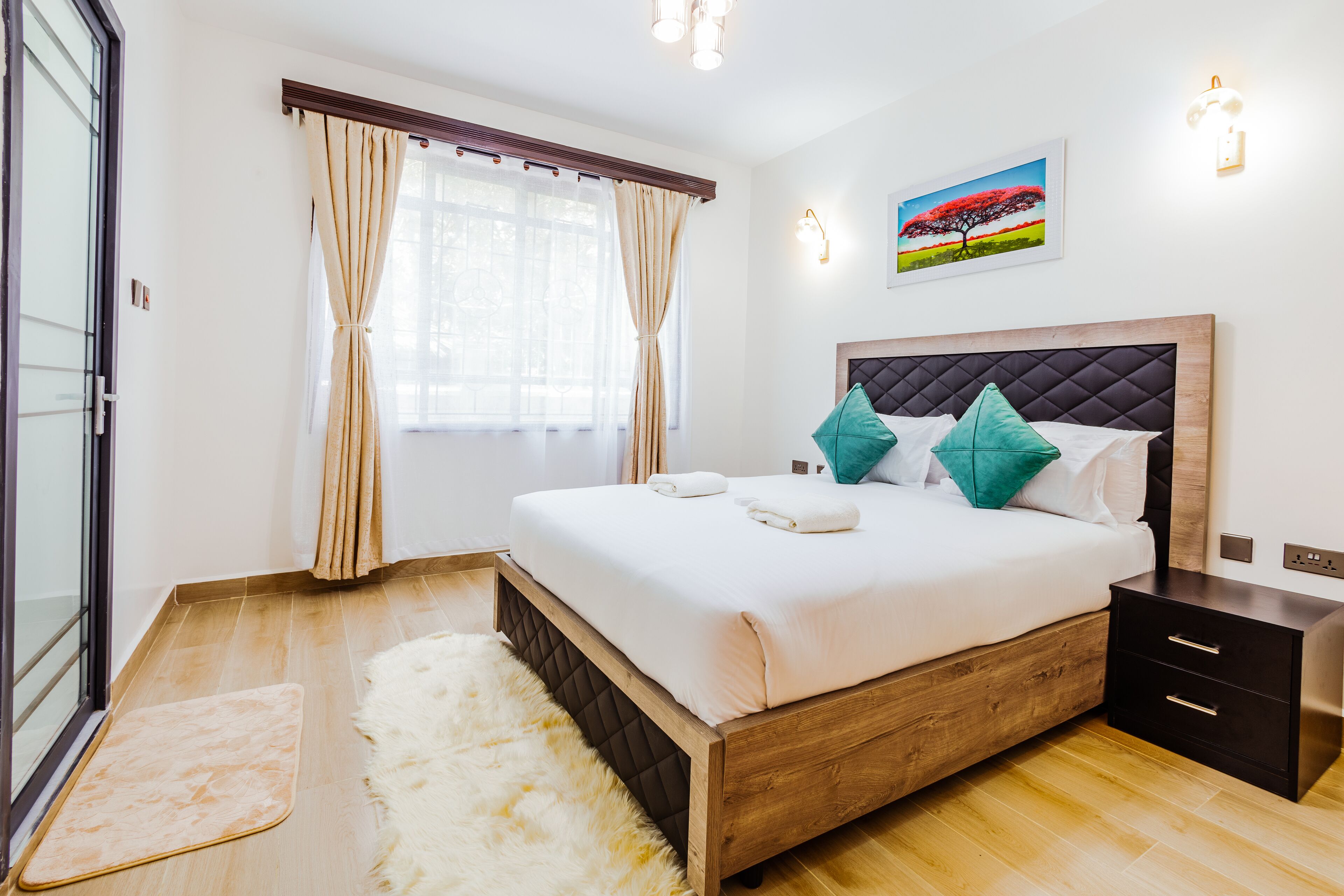 Une chambre moderne avec un lit en bois, une literie blanche, des coussins turquoise, un tapis moelleux, une table de chevet et un tableau au mur.
