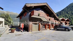A wooden building with a garage, a parking area, and a mountain backdrop. - Comfortable flat for 2 to 4 people, living room with 1 double divan bed, kitchen area with dishwashe (Grimentz)