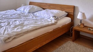A neatly made bed with white bedding and a wooden headboard in a room with wooden flooring and a small bedside table with a lamp. - Comfortable flat for 2 to 4 people, living room with 1 double divan bed, kitchen area with dishwashe (Grimentz)