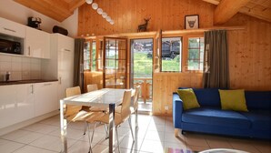 A wooden interior with a dining table, chairs, a blue sofa, and a kitchen area.
