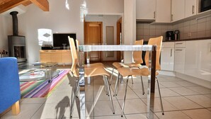 A modern kitchen with white cabinets, a tiled floor, and a dining area with a glass table and chairs.