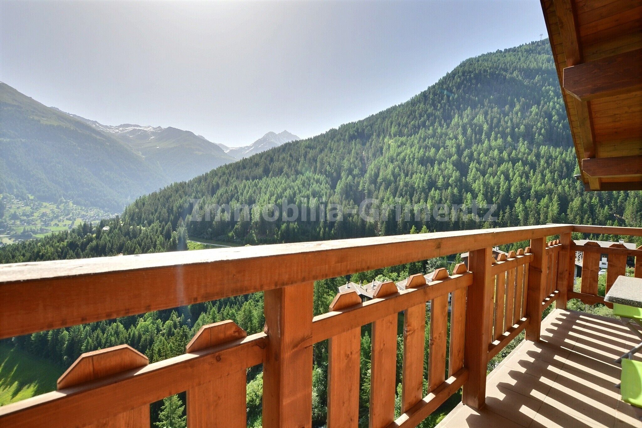 A wooden balcony with a view of a forested mountain range.